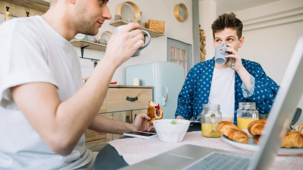 Deux adultes prennent un repas et des boissons devant un ordinateur