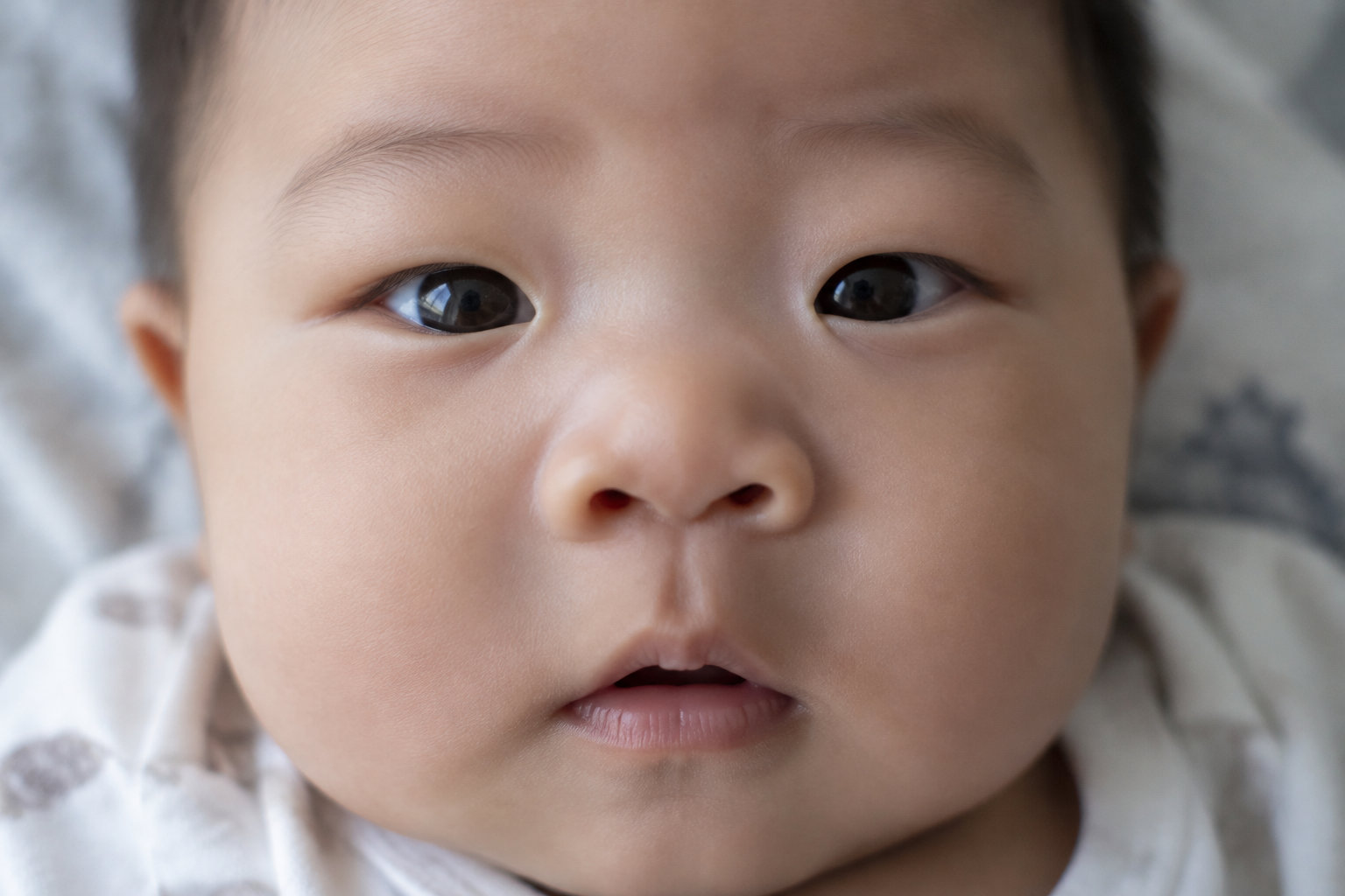 Gros plan sur le visage d’un bébé aux yeux foncés, vêtu d’un vêtement clair.